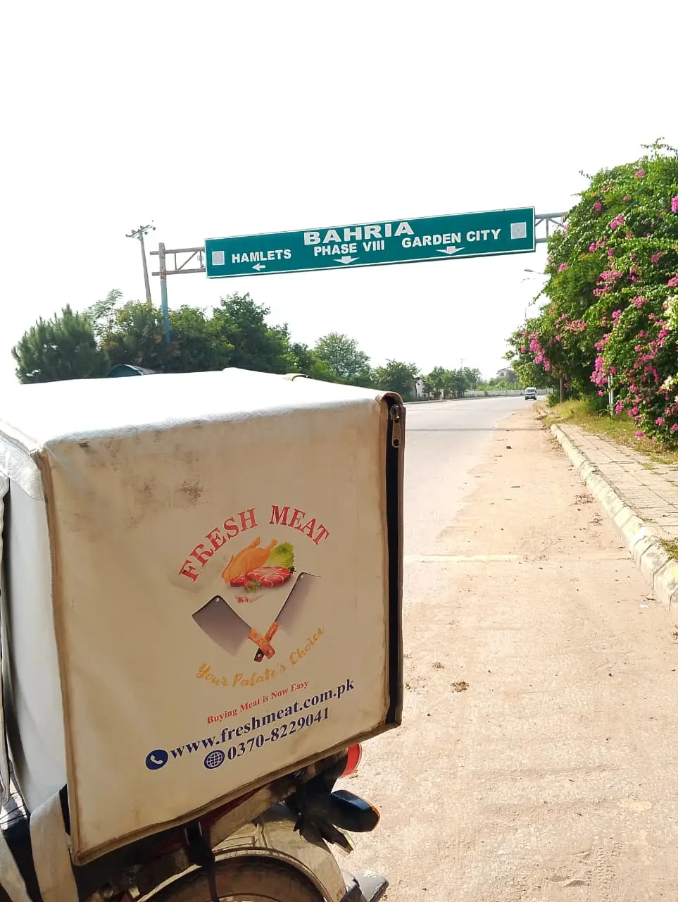 Bahria road sign pointing to Garden City, Phase VIII and Hamlets, with a Fresh Meat delivery bike